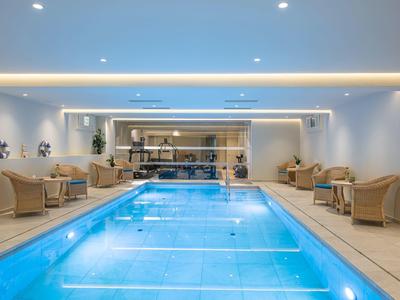 Piscina interna con sedie in vimini eleganti e illuminazione moderna luminosa.