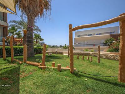 Grüner Garten mit Holzklettergerüsten in einem Hotel mit Palmen und blauem Himmel.