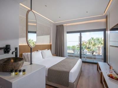 Modern hotelkamer met tweepersoonsbed, grote spiegel, terras en uitzicht op palmbomen.