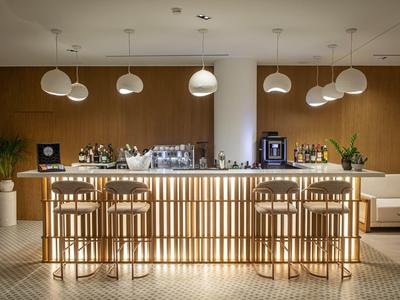 Area bar di hotel moderna con bancone in legno illuminato e sgabelli davanti a parete in legno