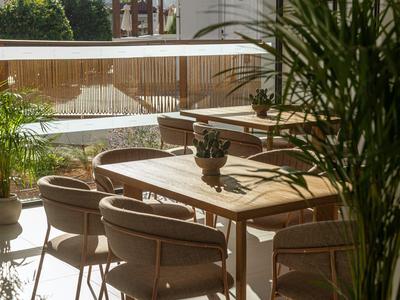 Terrassenbereich eines Hotels mit Holztischen, Stühlen und grünen Pflanzen.