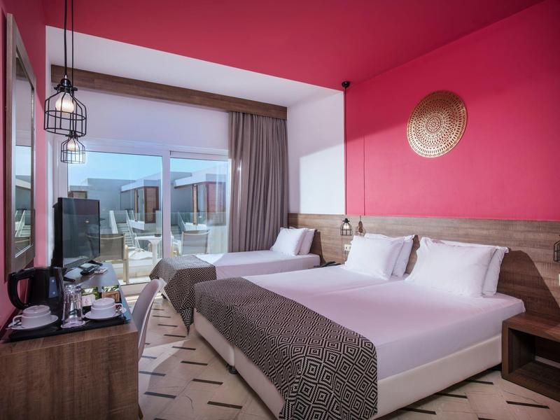 Habitación de hotel moderna con cama doble, alfombra de patrón de césped y vista a la terraza a la luz del día.