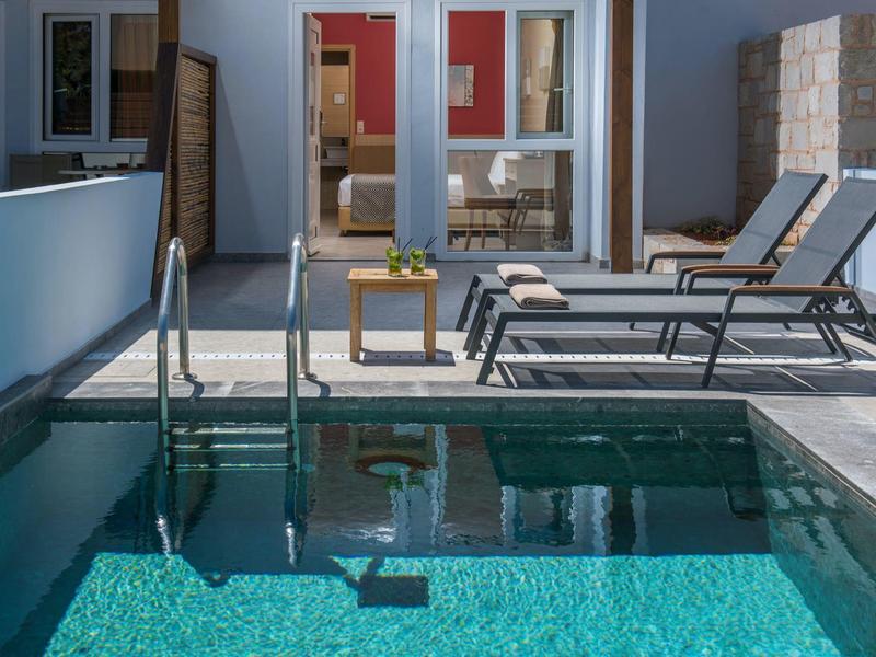 Piscina exterior moderna con tumbonas y mesa en la terraza de un hotel.