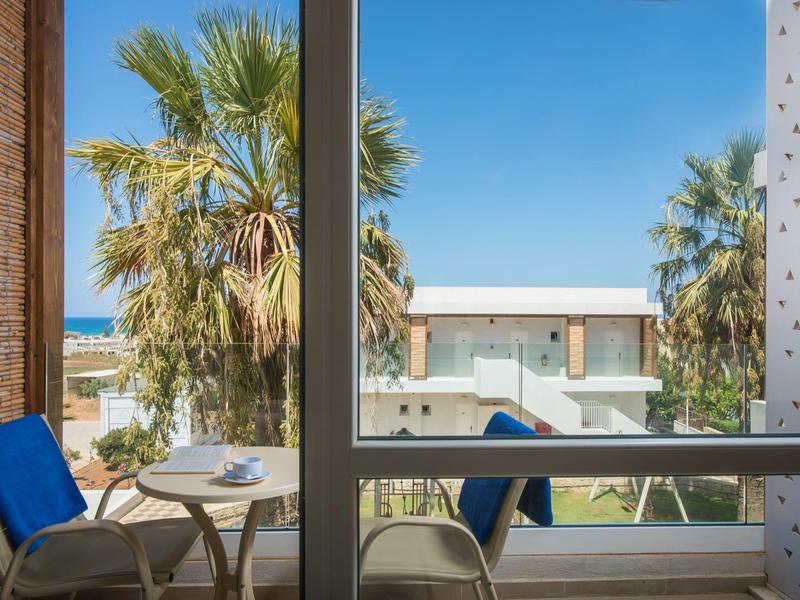 Vista desde el balcón del hotel con sillas, mesa y palmeras bajo un cielo despejado.
