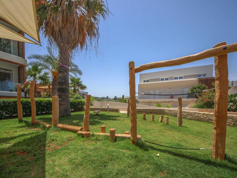 Área de juegos al aire libre con estructuras de madera en un hotel junto a palmeras y césped verde.