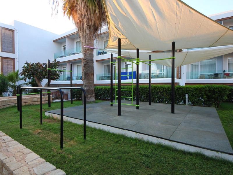 Área exterior techada con suelo de cemento y césped alrededor frente a un edificio de hotel.