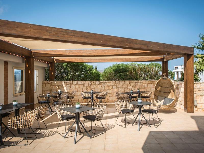 Terraza acogedora con mesas, sillas y pérgola de madera, rodeada de muros de piedra y plantas.