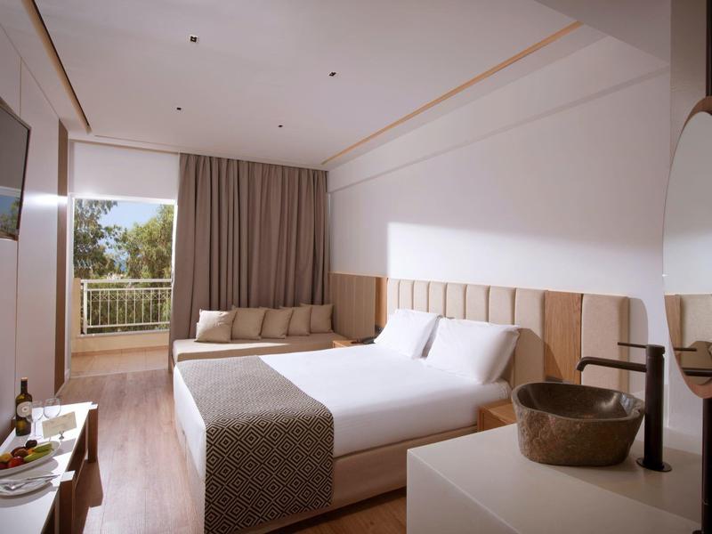 Habitación de hotel moderna con cama grande, balcón y decoración sencilla en tonos neutros.