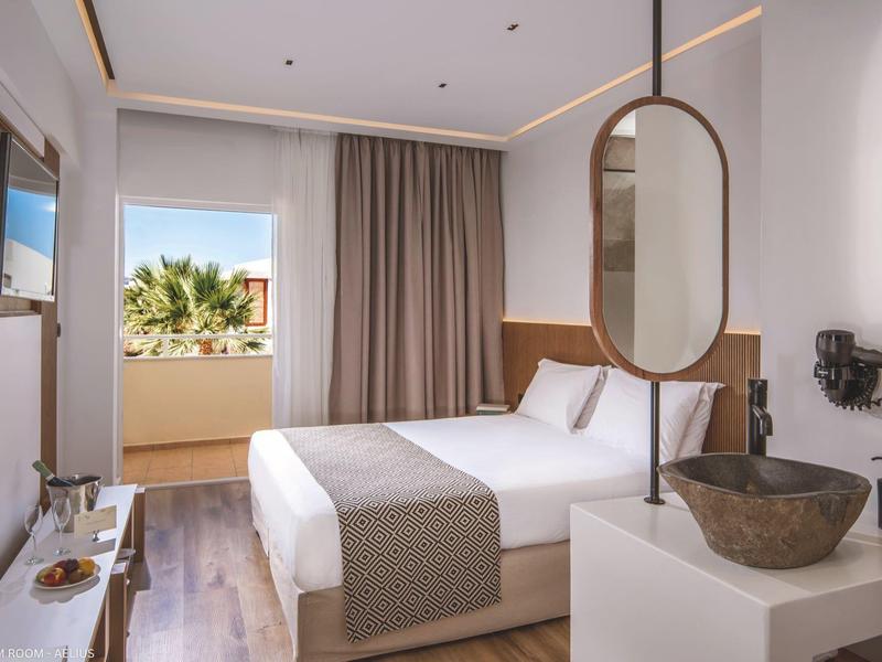 Habitación de hotel moderna con cama doble, gran espejo y balcón con vista a palmeras.