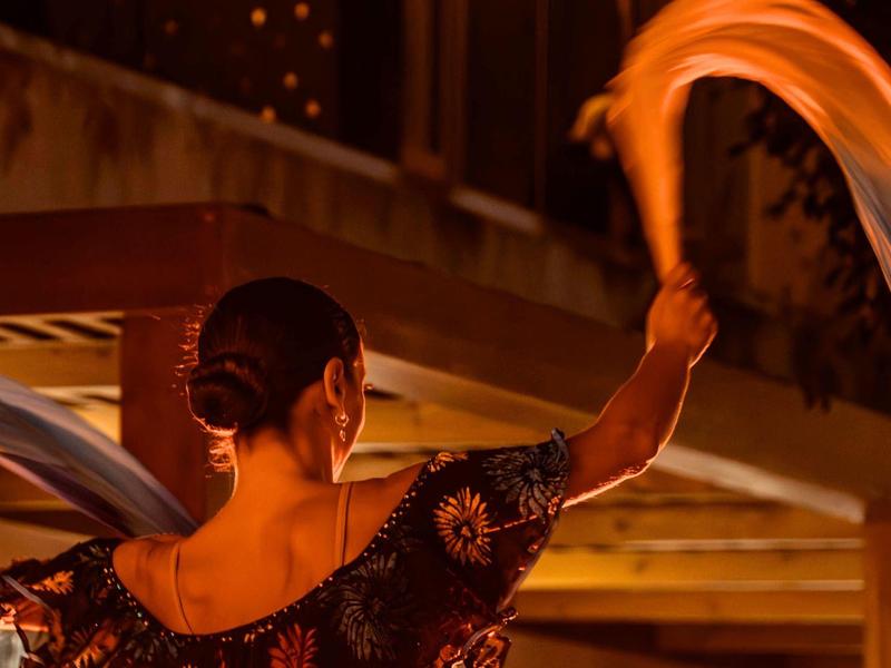 Mujer agita un pañuelo de noche frente a un restaurante o hotel iluminado.