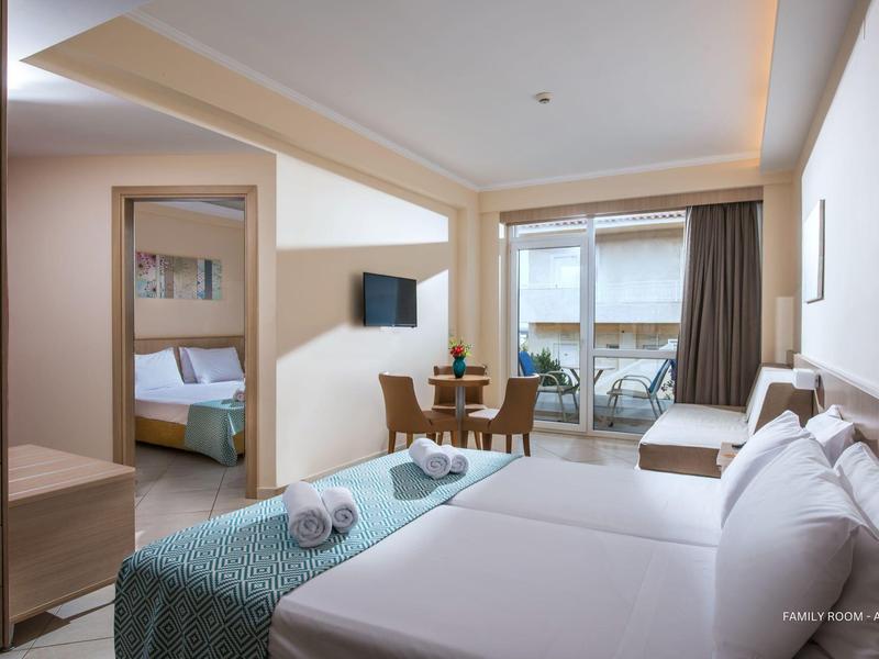 Habitación de hotel luminosa con cama doble, televisor, mesa de comedor, dormitorio contiguo y balcón.