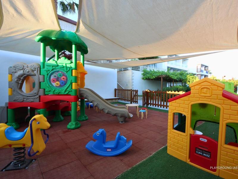 Área de juegos al aire libre con tobogán, columpios y casita en un complejo vacacional.