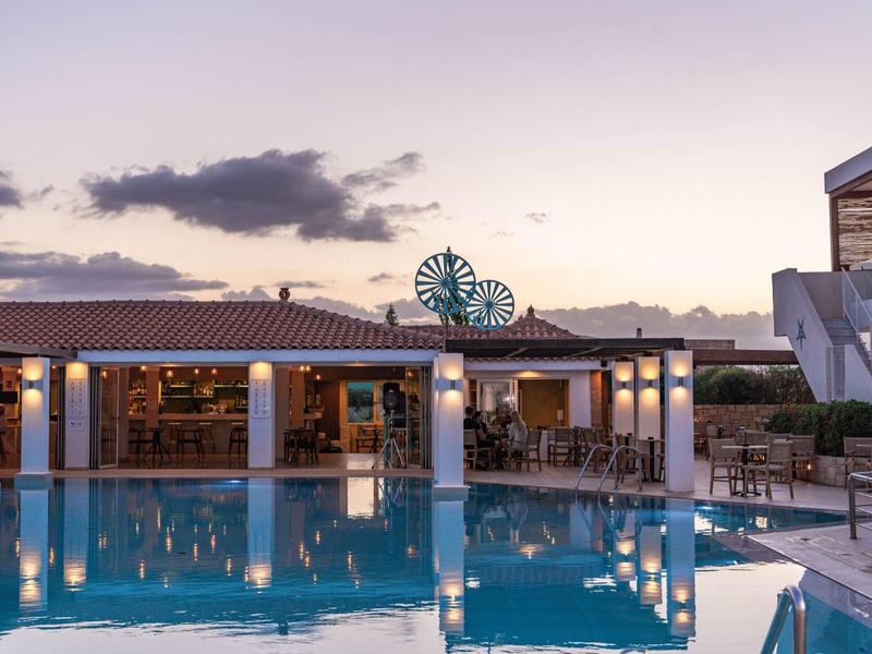 Área de piscina moderna con bar iluminado y asientos al atardecer.