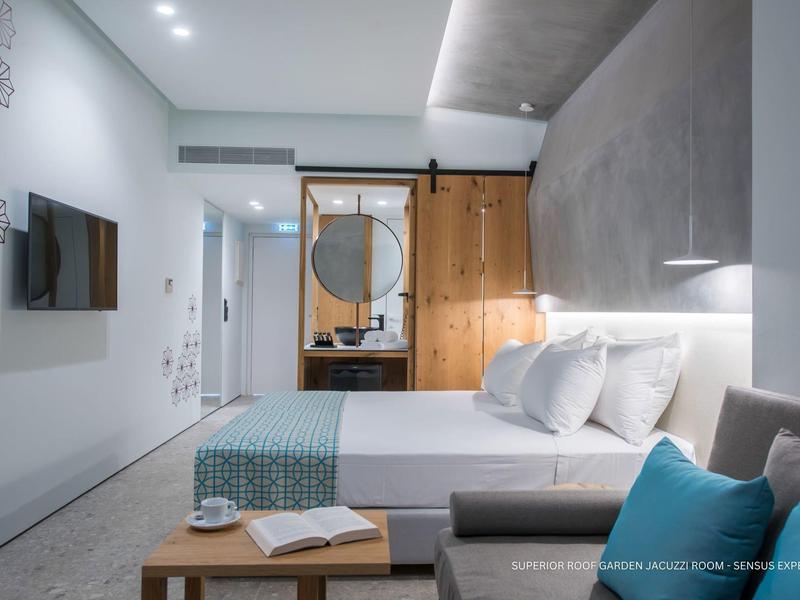 Habitación de hotel moderna con cama doble, puerta corredera de madera, sofá y televisor de pantalla plana.