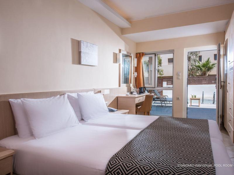 Habitación doble moderna con camas blancas, escritorio, balcón y vista a la piscina.