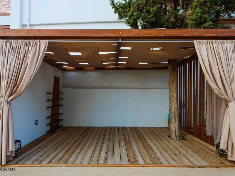 Pabellón moderno vacío de madera con cortinas y suelo de listones bajo el cielo abierto.