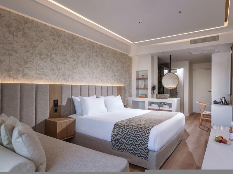 Camera d'hotel moderna con letto matrimoniale, divano, scrivania e illuminazione elegante.