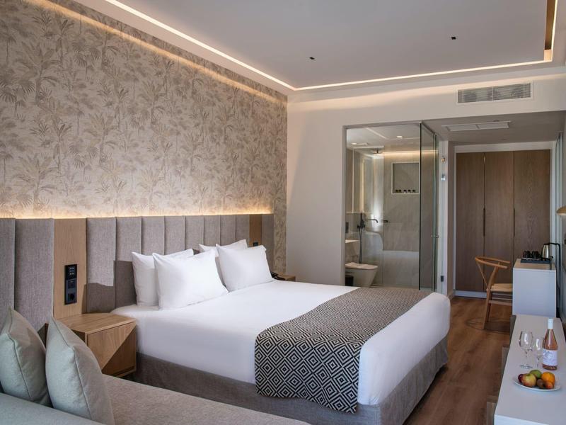 Camera d'hotel moderna con letto matrimoniale, bagno integrato e decorazioni neutre.