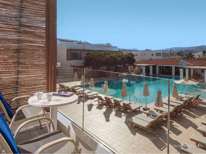 Balcone con sedie e tavolo che si affaccia sulla piscina dell'hotel e lettini al sole.