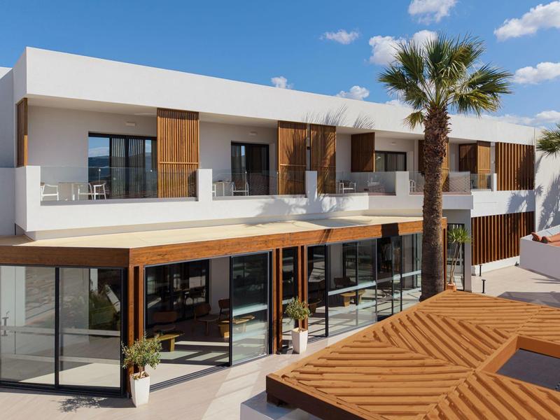 Hotel moderno con balconi, facciata in vetro e palme in una giornata di sole.