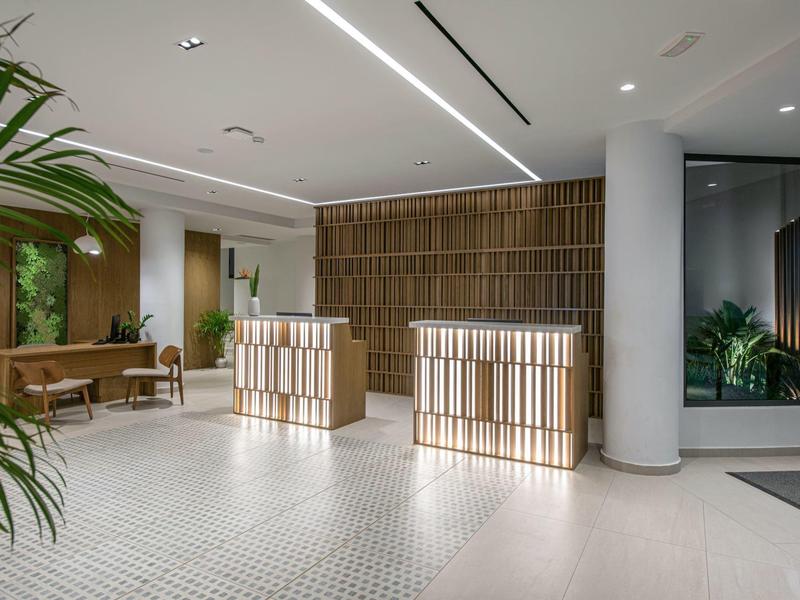 Hall moderno dell'hotel con pavimento chiaro, piante e scrivanie di legno alla reception.