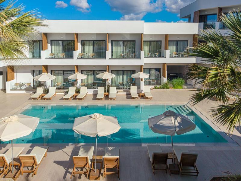 Area piscina moderna dell'hotel con lettini, tavoli e ombrelloni sotto un cielo blu.