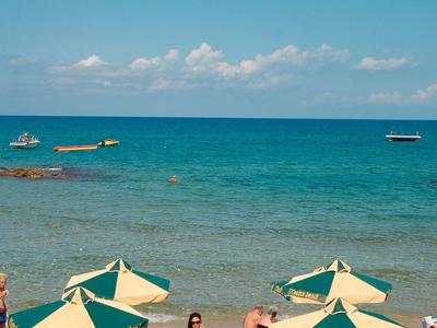 Strand mit gelb-grünen Sonnenschirmen, Menschen entspannen, türkisblaues Meer und blauer Himmel.
