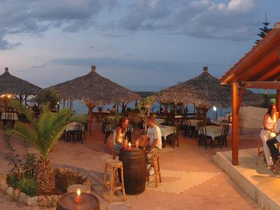 Strandbar bei Sonnenuntergang mit Strohdächern, Palmen und Gästen an Tischen und Bar.