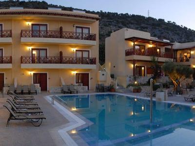 Hotel mit beleuchtetem Pool, Liegestühlen und Terrasse in den Abendstunden bei Bergkulisse.