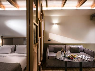 Chambre d'hôtel moderne avec lit double et coin salon confortable avec table et en-cas.