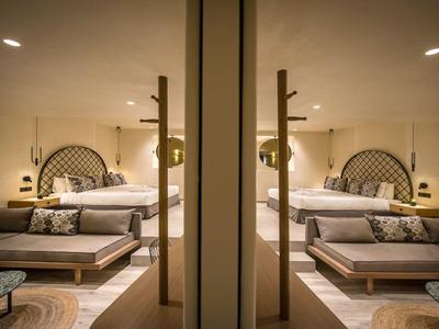 Chambre d'hôtel moderne avec grand lit, coin salon et lumière chaude.