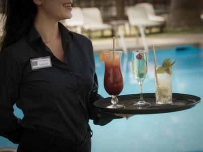 Kelnerka niesie tacę z trzema różnymi napojami przy basenie.