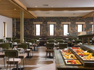 Salle à manger lumineuse avec chaises vertes et buffet de fruits et desserts.