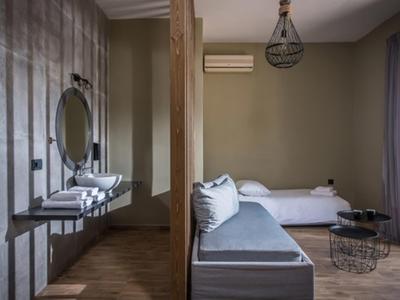 Chambre d'hôtel moderne avec canapé gris, lit et lampe minimaliste au plafond.