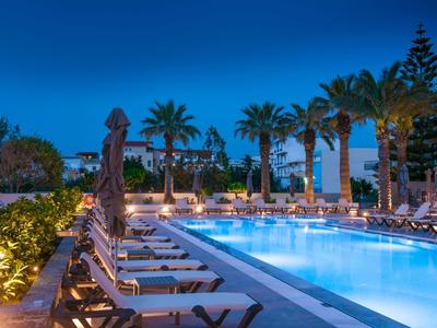 Piscina de hotel iluminada con numerosas tumbonas y palmeras al anochecer.
