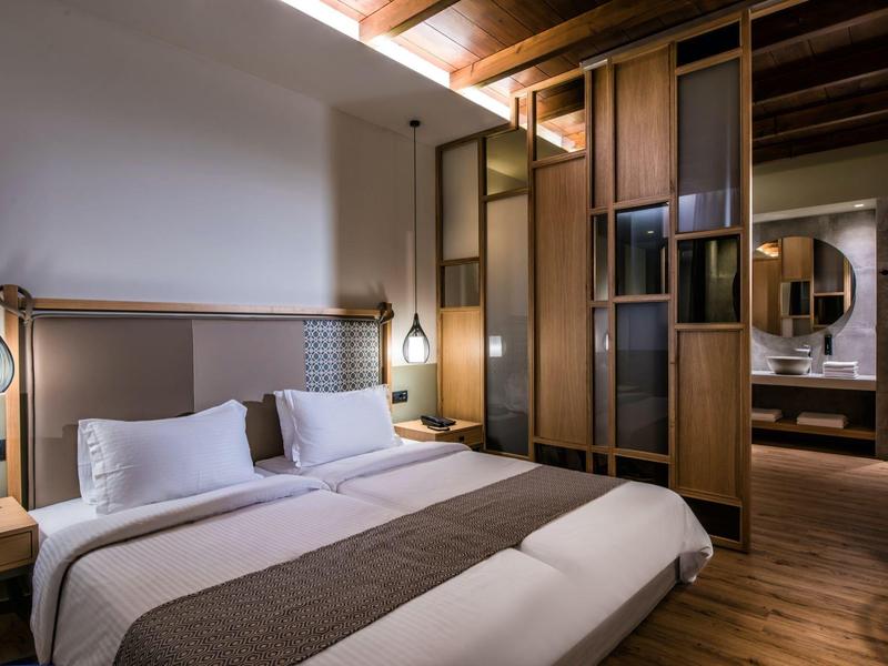 Chambre d'hôtel moderne avec grand lit, boiseries et éclairage indirect.