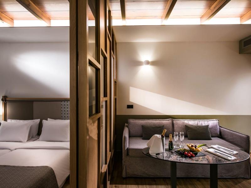 Chambre d'hôtel moderne avec lit double et coin salon confortable avec table et en-cas.