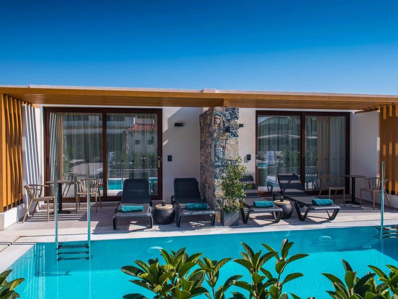 Espace hôtelier moderne avec piscine, chaises longues et deux grandes fenêtres sous un ciel clair.