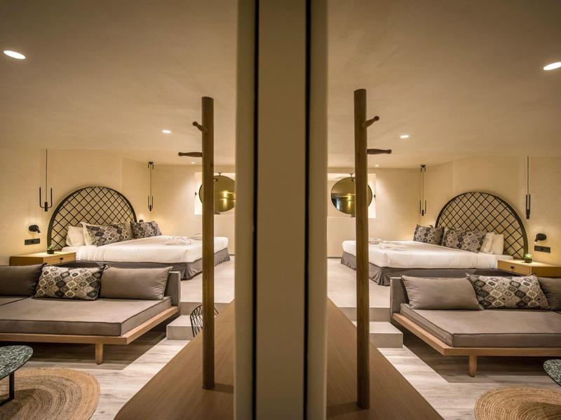 Chambre d'hôtel moderne avec grand lit, coin salon et lumière chaude.