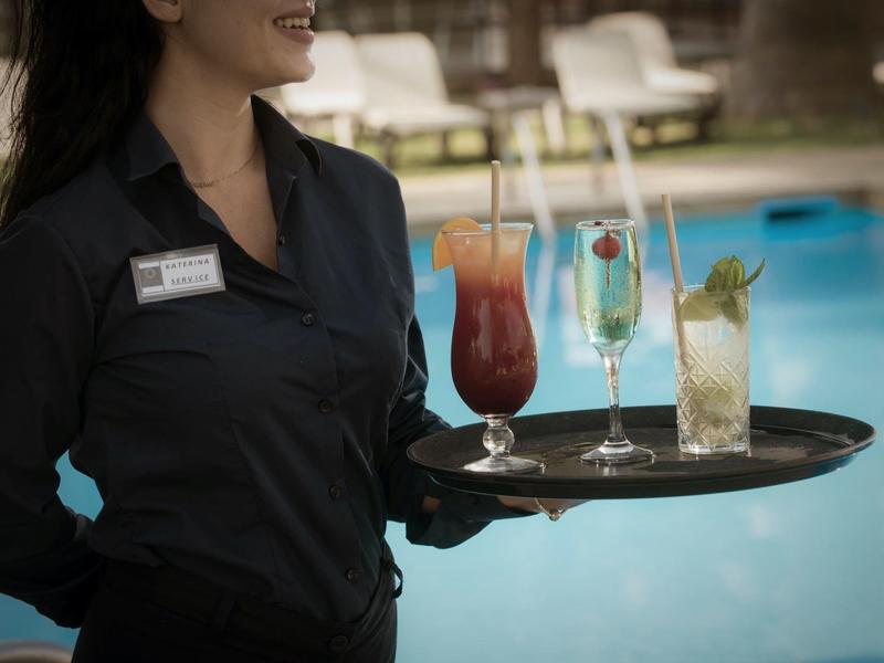 Serveuse porte un plateau avec trois cocktails colorés au bord de la piscine.