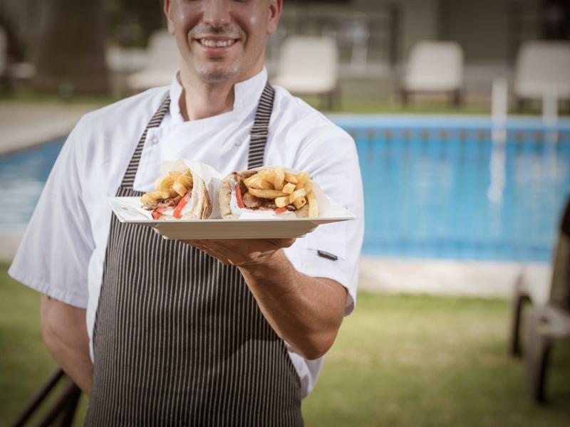 Un chef présente deux sandwichs sur une assiette blanche devant une piscine.