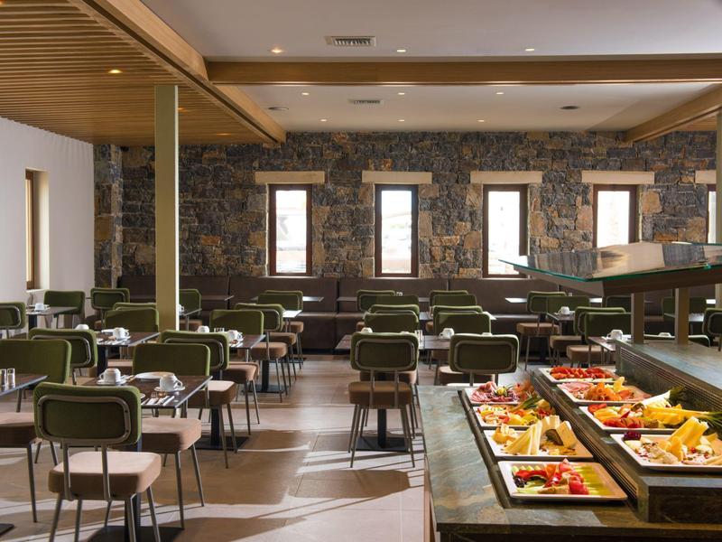 Salle à manger lumineuse avec chaises vertes et buffet de fruits et desserts.