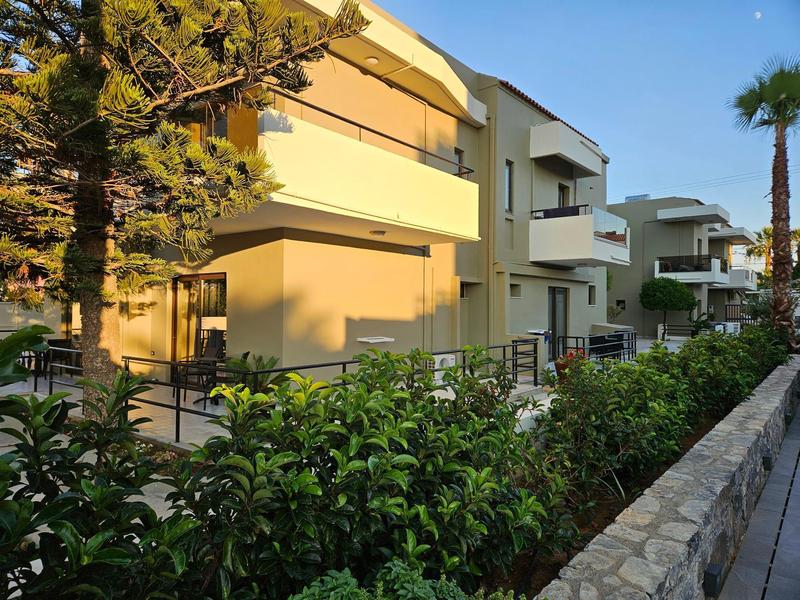Maisons de vacances modernes avec balcons, entourées de buissons verts et de palmiers au coucher du soleil.