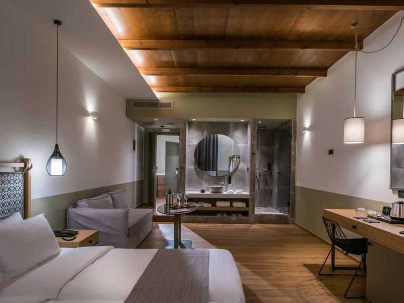 Chambre d'hôtel moderne avec plafond en poutres, lit, canapé et coin bureau.