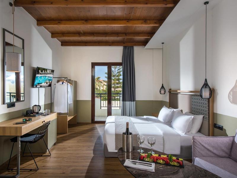 Chambre d'hôtel moderne avec plafond à poutres en bois, lit, bureau et balcon.
