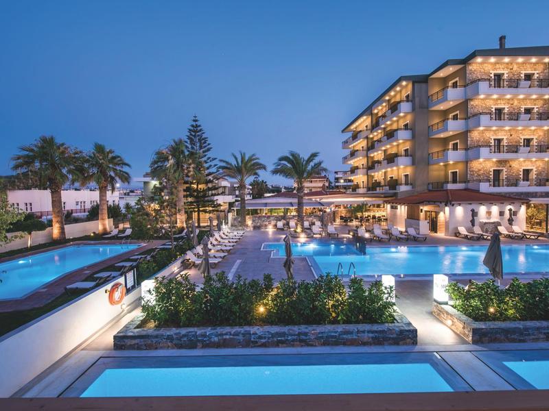 Complex hôtelier moderne avec piscine illuminée et palmiers au crépuscule.