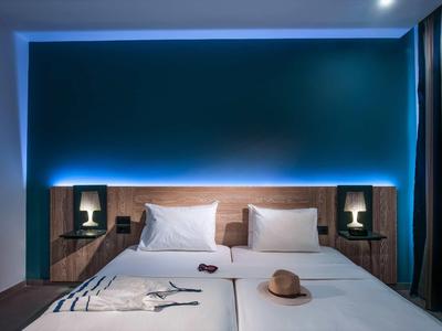 Modern hotel room with two single beds, night lamps, and blue backlighting