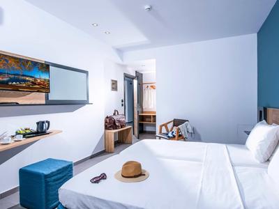 Modern hotel room with double bed, blue stool, desk, and open wardrobe.