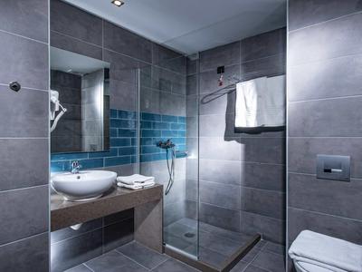 Modern bathroom with gray tiles, glass shower, sink, and towels.