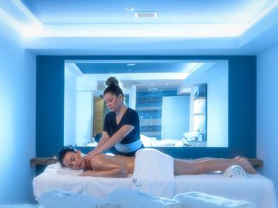 Woman receives massage on white massage table in calm, blue-lit room.